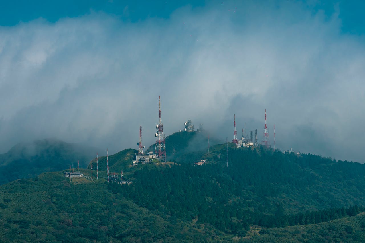 Aerial view of communication towers on a misty mountain peak surrounded by lush greenery.